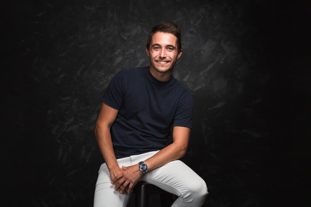 portrait d'un jeune homme souriant sur un tabouret faite par un photographe professionnel en studio