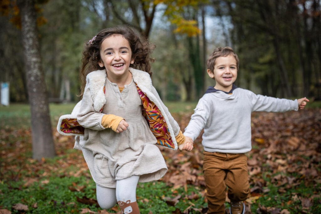 photo de 2 enfants courant main dans la main réalisée séance photo enfant en extérieur par un photographe professionnel à Annecy à l'automne