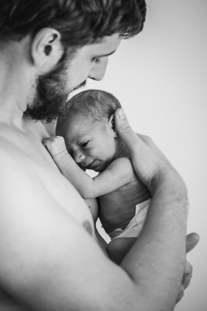 photo d'un nouveau né à l'allaitement dans les bras de son papa réalisée à domicile par un photographe professionnel à Annecy