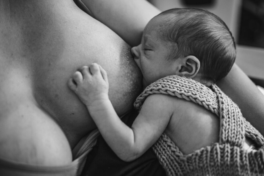 photo d'un nouveau né à l'allaitement dans les bras de sa maman réalisée à domicile par un photographe professionnel à Chambéry