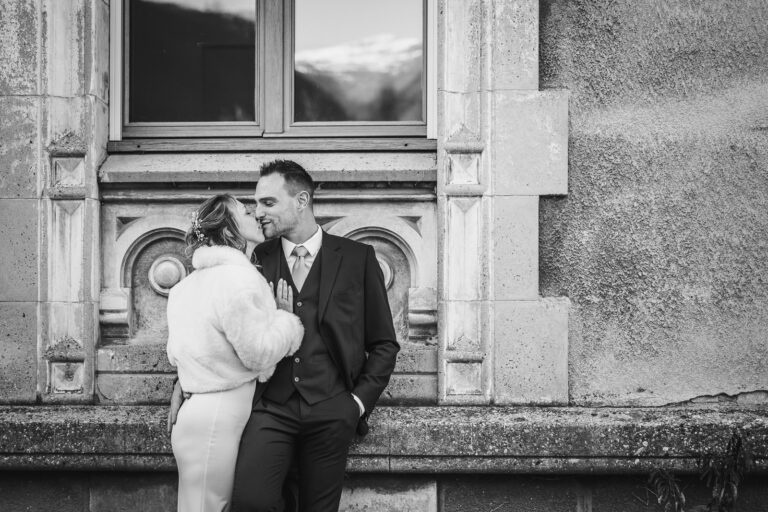 couple de mariés adossé au mur d'un château, les mariés s'embrassent, photo réalisée par un photographe mariage à Chambéry