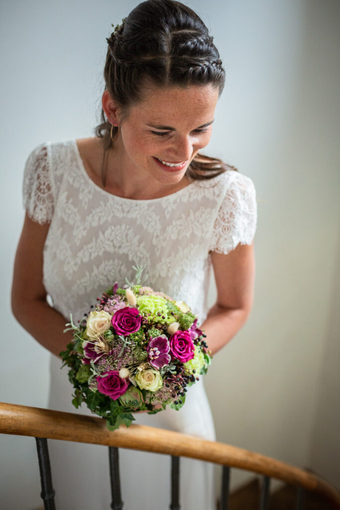 portrait de la mariée souriante avec son bouquet de fleur dans les escaliers de la maison où elle s'est préparée