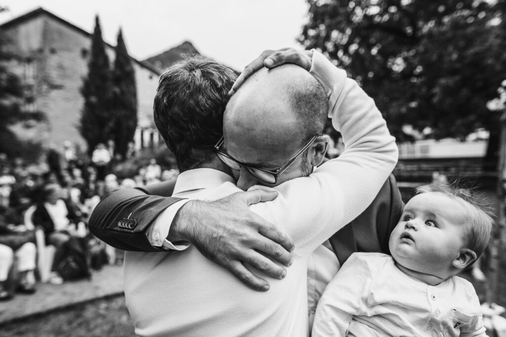 photo pleine d'émotion lors d'une cérémonie de mariage où le témoin et la marié se prennent dans les bras, photo prise par un photographe reportage mariage sur le vif