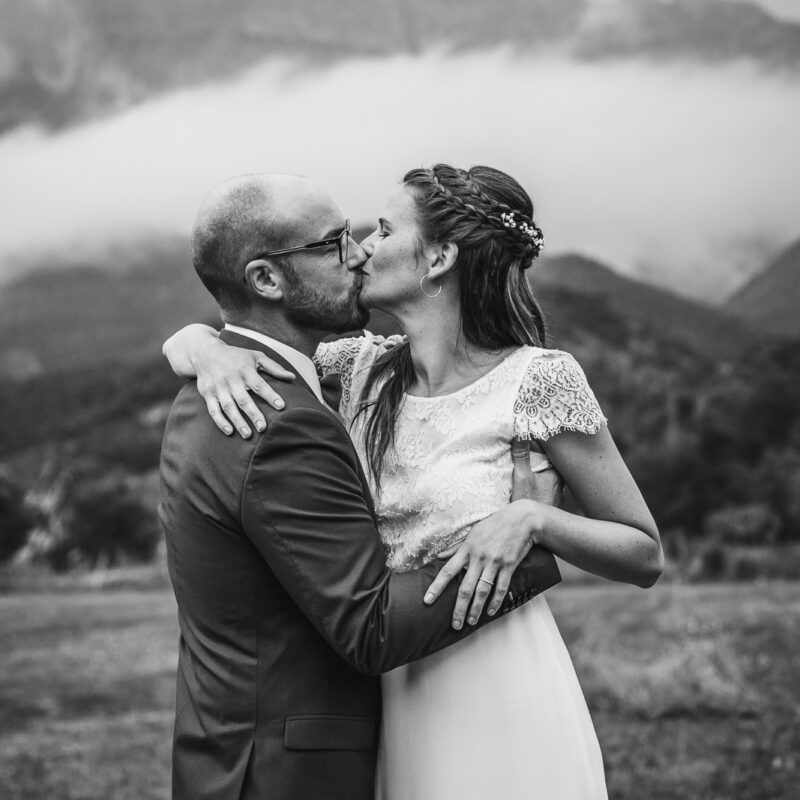 les mariés s'embrassent lors de leur séance couple le jour de leur mariage, avec en fond un paysage montagne magnifique