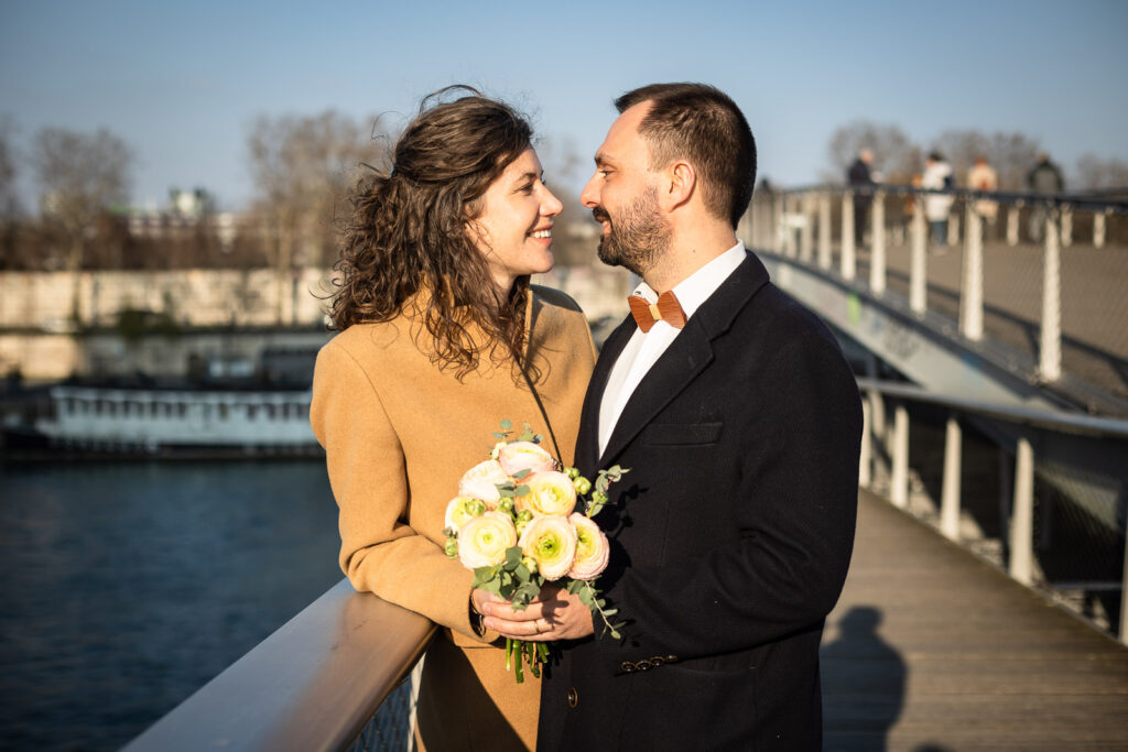 couple s'embrassant tendrement appuyé sur la rambarde d'un pont à Paris, lors d'une séance photo avec un photographe professionnel
