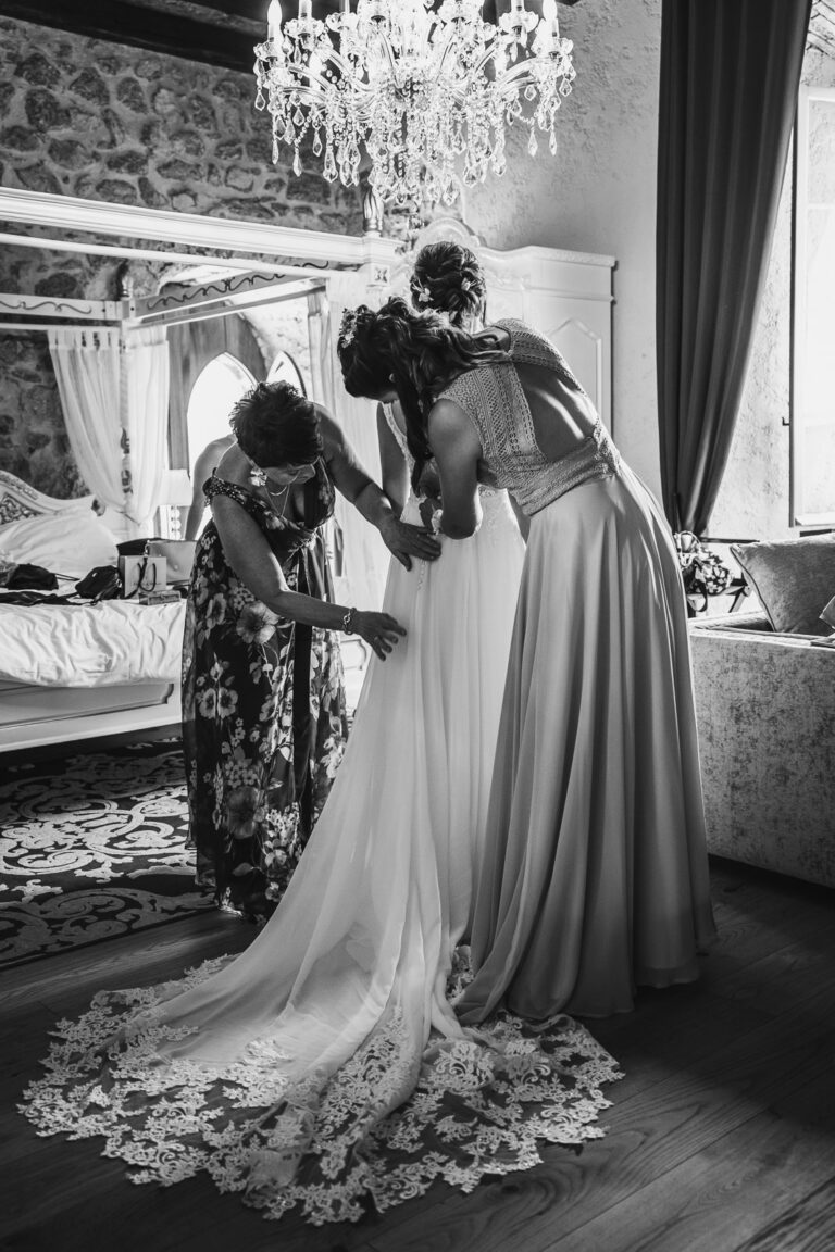 mariée lors de ses prépartifs dans la suite d'un chateau, aidée par ses proches pour ajuster sa robe de mariée